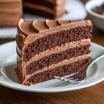 A luscious slice of Chocolate Mousse Cake Recipe featuring three layers of moist chocolate sponge and creamy mousse, served on a white plate.