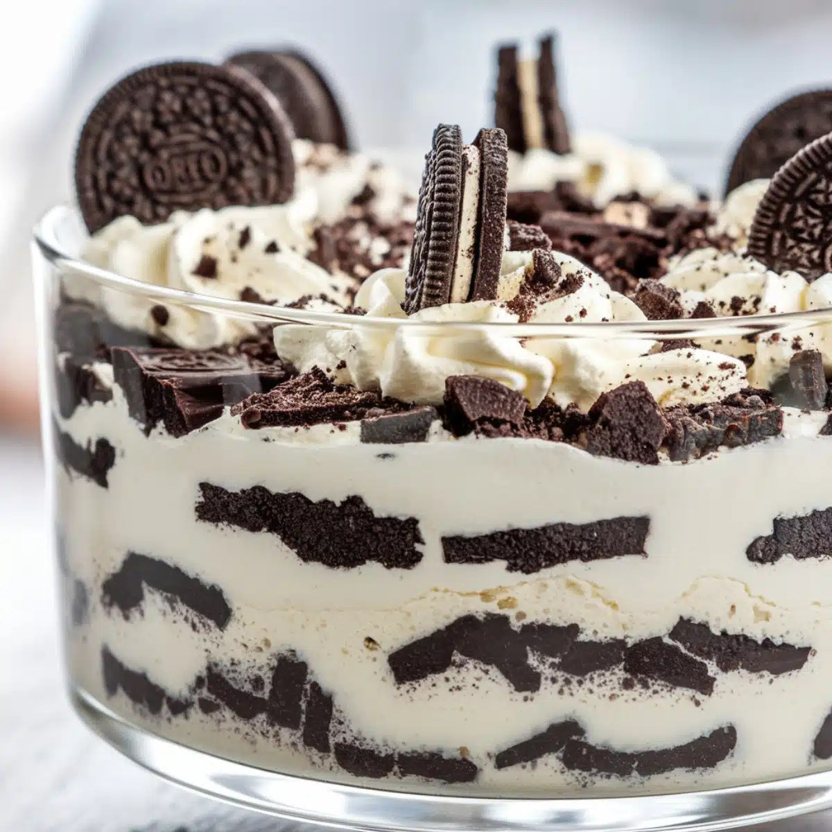 A glass bowl filled with layers of crushed Oreos, whipped cream, and cream cheese filling, topped with whole Oreo cookies and crumbled pieces, showcasing a decadent Oreo Dirt Cake Recipe.