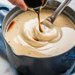 A rich and creamy mixture being stirred in a saucepan while vanilla extract is poured in, an essential step in making a smooth and flavorful Brownie Frosting Recipe. The glossy texture of the frosting ensures a luscious topping for decadent homemade brownies.