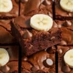 A close-up of rich, fudgy Banana Brownie Recipe cut into squares, topped with chocolate chips and fresh banana slices. The brownies have a moist, dense texture with a glossy, crackly top, highlighting the perfect combination of chocolate and banana flavors. These decadent homemade brownies are an indulgent twist on a classic dessert.