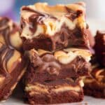 A stack of Cream Cheese Brownies Recipe featuring a rich, fudgy chocolate base and a luscious, swirled cheesecake topping. These decadent brownies have a gooey texture with melted chocolate and a creamy cheesecake layer, making them an irresistible dessert for chocolate lovers.