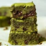 Stack of rich and fudgy Matcha Brownies Recipe, featuring a vibrant green hue from high-quality matcha powder and gooey melted chocolate chunks. The brownies have a soft, moist texture with slightly crisp edges, making them the perfect blend of earthy matcha flavor and deep chocolate richness. Placed on parchment paper, these matcha brownies create an irresistible and indulgent dessert scene.