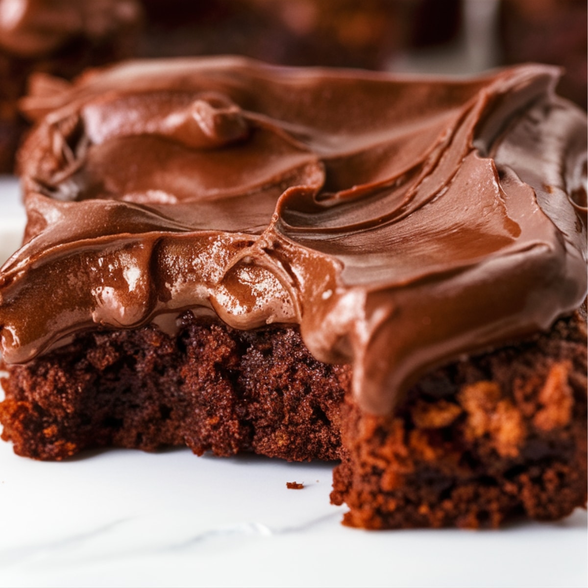 A rich and fudgy brownie topped with a smooth, creamy chocolate frosting. The glossy texture of the frosting highlights its velvety consistency, making it the perfect finishing touch for any Brownie Frosting Recipe. The decadent chocolate topping swirls beautifully over the moist brownie base, creating an irresistible homemade dessert.