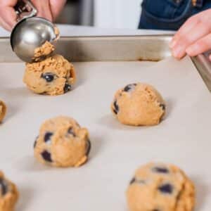 Monster Cookies Recipe – Scooping perfectly portioned cookie dough with chocolate chips onto a parchment-lined baking sheet, ready to bake into chewy, delicious treats.