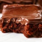 A close-up of a fudgy brownie topped with a rich, velvety chocolate frosting. The glossy and smooth texture of the frosting melts over the moist brownie, making it the perfect Brownie Frosting Recipe for chocolate lovers. This indulgent dessert is a must-try for anyone craving a homemade, decadent chocolate treat.