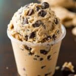 Homemade chocolate chip Edible Cookie Dough scooped into a clear plastic cup, packed with melty chocolate chips and a rustic, hand-scooped texture.