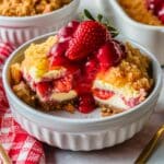 A bowl of Strawberry Cheesecake Dump Cake with a golden crumb topping, creamy cheesecake layers, and glossy strawberry sauce, garnished with fresh strawberries.