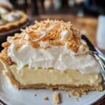 A slice of homemade coconut cream pie with a flaky graham cracker crust, creamy coconut filling, whipped cream topping, and toasted coconut flakes, served on a dessert plate.