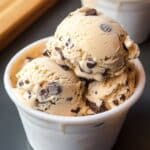 Homemade cookie dough ice cream with chocolate chips in a white paper cup, showing soft, hand-scooped texture and slight melting at the edges.