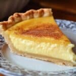 Homemade egg custard pie slice with a flaky crust and creamy yellow filling, topped with nutmeg, on a vintage floral plate.