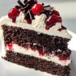 Homemade Black Forest Cake slice with moist chocolate layers, whipped cream, cherry filling, and topped with fresh cherries and chocolate curls.