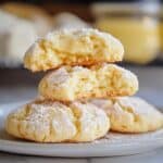 Homemade gooey butter cookies stacked on a plate, dusted with powdered sugar, with one broken open to reveal a soft, creamy center. Warm, cozy kitchen vibes in the background.