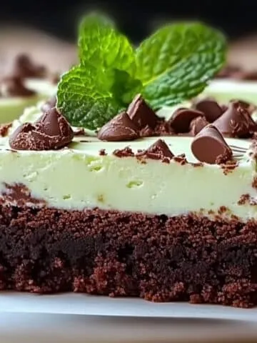 Homemade mint brownies with a fudgy chocolate base, creamy mint frosting, topped with chocolate chips and a fresh mint sprig, set on parchment paper.