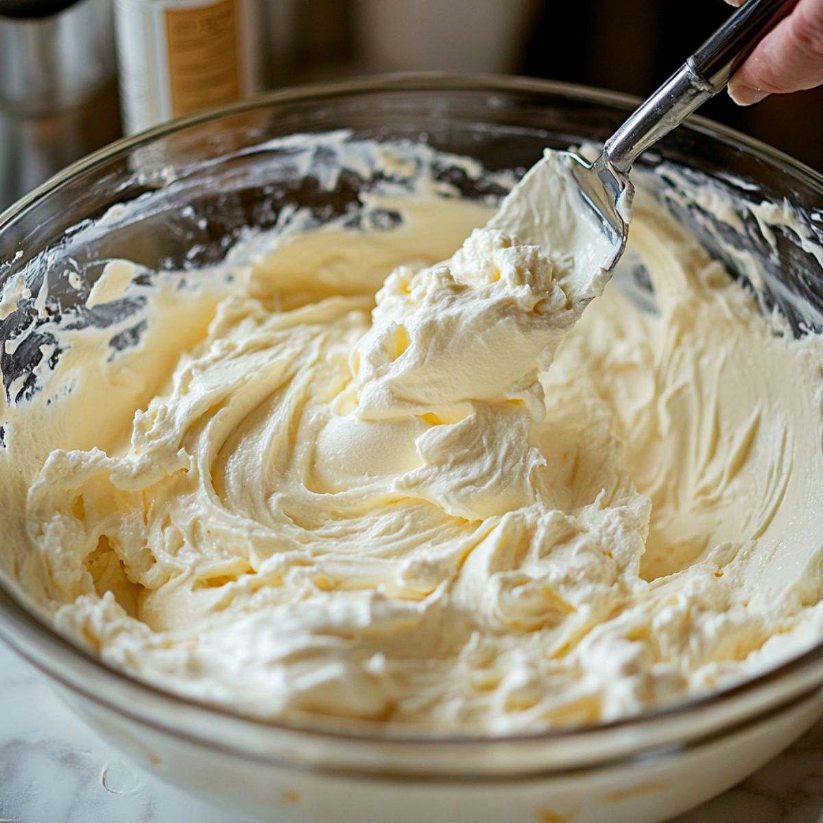 Close-up of creamy Butterfinger Pie filling in a glass bowl, with a spatula lifting a fluffy scoop, all naturally lit in a real kitchen setting.