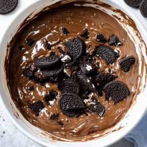 Brownie batter in a bowl topped with crushed Oreo cookies, ready to mix.