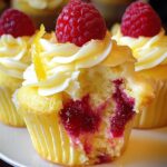 Homemade Lemon Raspberry Cupcakes filling, topped with lemon buttercream, a fresh raspberry, and candied lemon peel, shown with a bite revealing the juicy center.