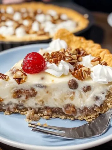 Slice of homemade million dollar pie with creamy filling, pecans, whipped cream, and a cherry on top, served on a blue plate.