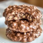 Stack of three homemade no bake cookies with nuts, one bitten to reveal a fudgy, nutty center on a white plate.