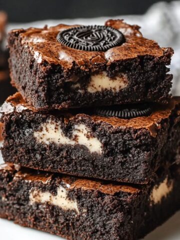 Stack of three fudgy, homemade Oreo brownies with a crackly top, creamy Oreo chunks inside, and a whole Oreo baked into the top brownie.