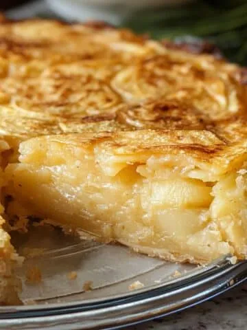 Homemade Passover potato pie with a golden crust and creamy potato filling, served in a glass dish with one slice removed.