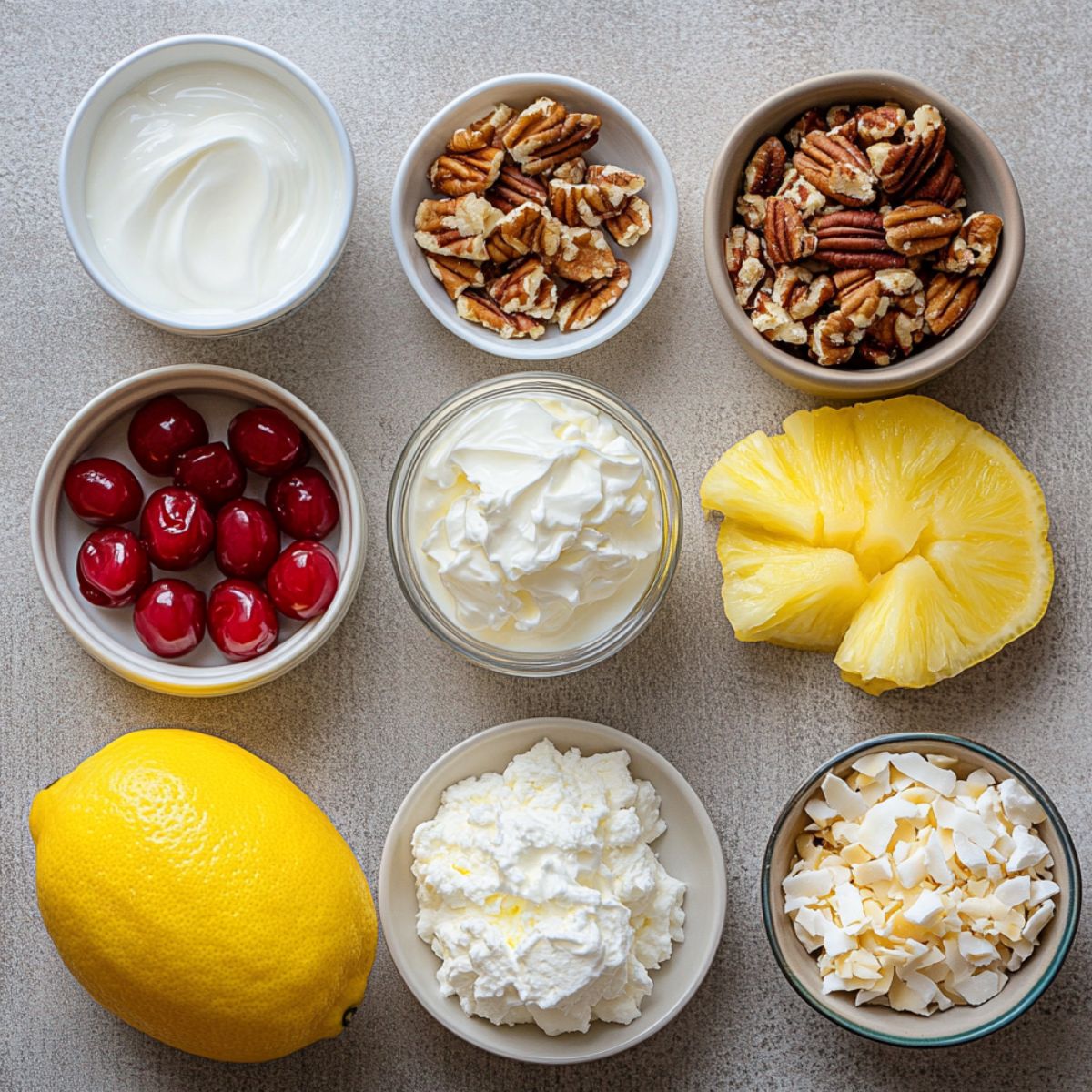 Ingredients for homemade million dollar pie, including cherries, pecans, pineapple, whipped cream, coconut, and a lemon, arranged on a countertop.