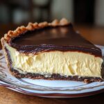 Homemade Boston cream pie slice with rich chocolate ganache, creamy vanilla custard, and a rustic chocolate crust on a decorative plate.