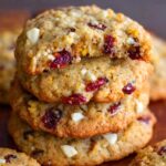 Stack of homemade cranberry orange cookies with white chocolate chunks, golden edges, and a soft, chewy center. Top cookie has a bite taken out, showing cranberries and zest inside.