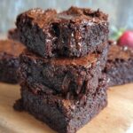 Stack of rich, Homemade Gluten Free Brownies with a crackly top and gooey melted chocolate, sitting on a wooden board.