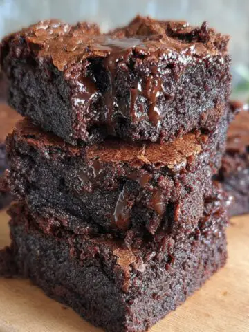 Stack of rich, Homemade Gluten Free Brownies with a crackly top and gooey melted chocolate, sitting on a wooden board.