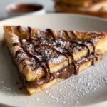 Homemade Nutella Toast Pies cut into a triangle, filled with gooey Nutella, dusted with powdered sugar, and drizzled with chocolate on a plate.