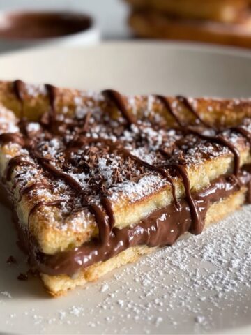 Homemade Nutella Toast Pies cut into a triangle, filled with gooey Nutella, dusted with powdered sugar, and drizzled with chocolate on a plate.