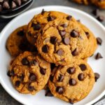 Homemade pumpkin chocolate chip cookies stacked on a white plate, golden and soft with melty chocolate chips and a rustic, cozy look.