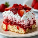 A slice of homemade strawberry tres leches cake with moist vanilla sponge, strawberry compote, pink cream, whipped topping, and fresh strawberry slices on a ceramic plate.