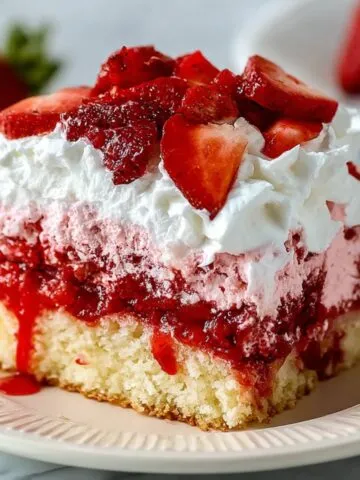 A slice of homemade strawberry tres leches cake with moist vanilla sponge, strawberry compote, pink cream, whipped topping, and fresh strawberry slices on a ceramic plate.