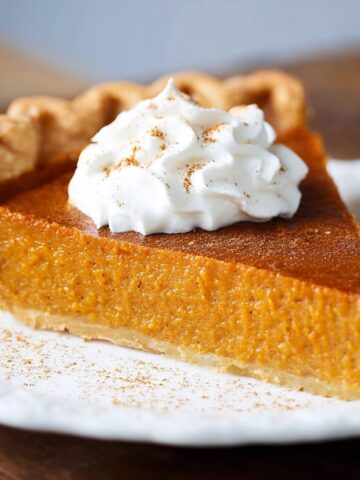 Homemade slice of sweet potato pie with flaky crust, whipped cream, and cinnamon on a white plate.