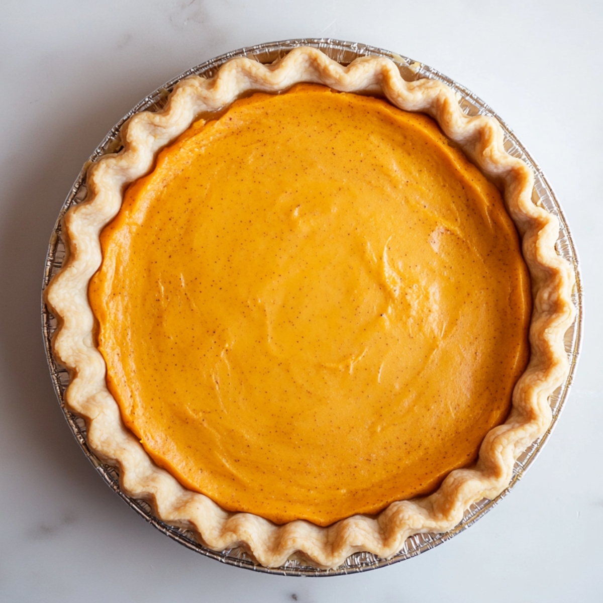 Unbaked homemade sweet potato pie with smooth orange filling in a fluted pie crust, ready to go into the oven.