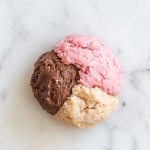 A scoop of chocolate, vanilla, and strawberry cookie dough on a white marble surface.