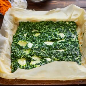 Unbaked spinach pie in a parchment-lined dish, with creamy spinach and cheese filling spread over a phyllo base, ready for baking.