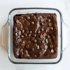 Freshly baked black bean brownies in a square glass dish, topped with melty chocolate chips on a glossy, crackled surface.