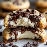 Stacked homemade Cheesecake Stuffed Chocolate Chip Cookies split in half, revealing creamy cheesecake filling and melted chocolate chunks. Golden-brown cookie edges with scattered chocolate chips on parchment paper.