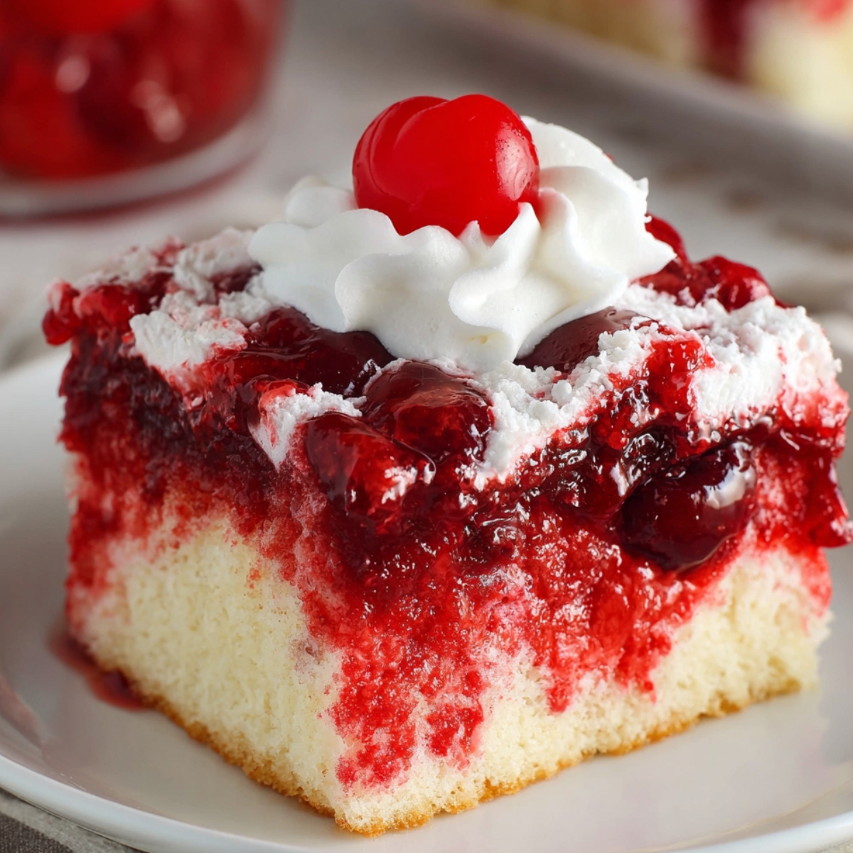 Moist homemade cherry poke cake slice with whipped cream and cherry topping, served on a white plate with a gold fork.