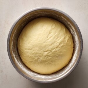 Homemade enriched yeast dough fully risen in a metal mixing bowl, ready to be rolled for strawberry cheesecake cinnamon rolls.