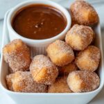 Homemade air fryer churro bites coated in cinnamon sugar, served in a white square dish with a ramekin of thick chocolate dipping sauce.