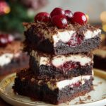 Homemade Black Forest brownies stacked on a plate, with layers of fudgy chocolate, cherry filling, whipped cream, and topped with cherries and chocolate shavings.
