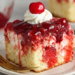 Homemade cherry poke cake slice with cherry filling, whipped cream, and a maraschino cherry on top.
