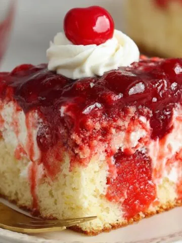 Homemade cherry poke cake slice with cherry filling, whipped cream, and a maraschino cherry on top.