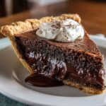 Slice of homemade chocolate pie with gooey center, flaky crust, and whipped cream on top.