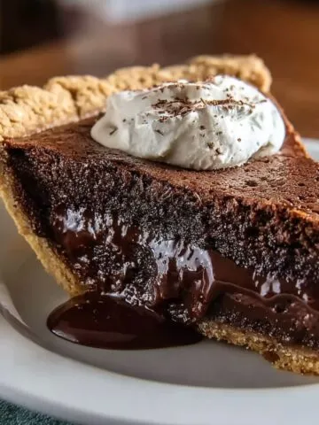 Slice of homemade chocolate pie with gooey center, flaky crust, and whipped cream on top.