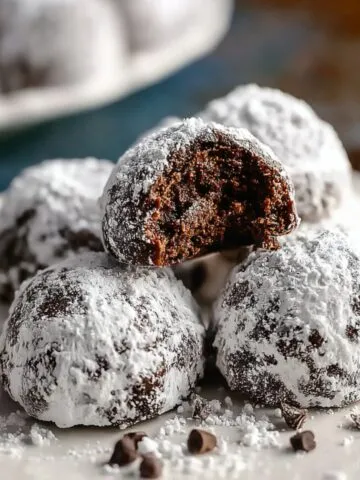 Homemade chocolate snowball cookies coated in powdered sugar on a plate, with one broken open to show the rich, fudgy center and natural cracks.