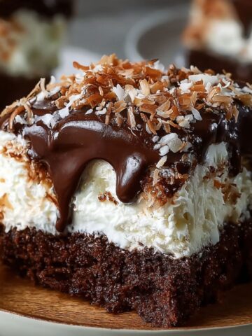 A homemade slice of Mounds Cake with moist chocolate cake, a thick coconut filling, rich chocolate ganache dripping down the sides, and toasted coconut sprinkled on top, served on a plate with a fork.